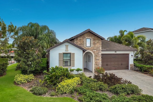 view of front facade with a garage, decorative driveway, stone siding, and stucco siding