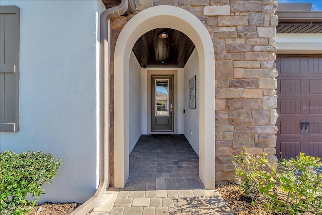 property entrance with a garage, stone siding, and stucco siding