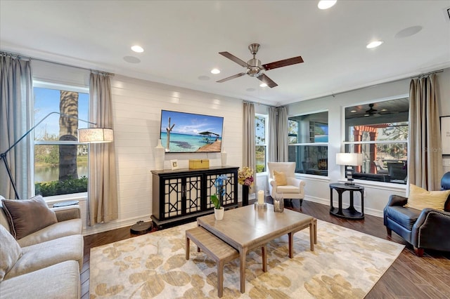 living area with recessed lighting, a ceiling fan, wood walls, wood finished floors, and baseboards