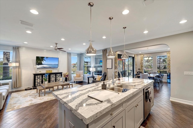 kitchen with decorative light fixtures, open floor plan, a sink, an island with sink, and light stone countertops