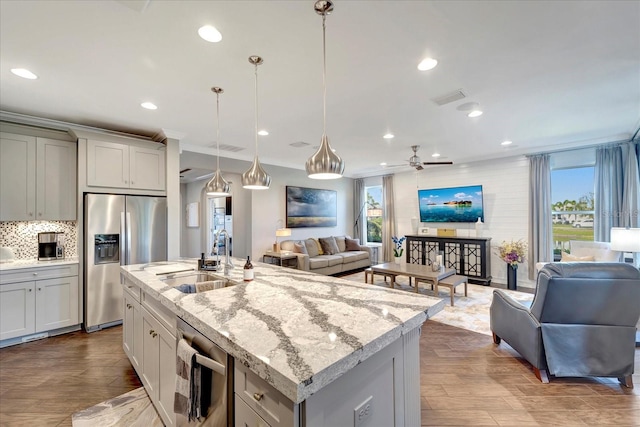 kitchen featuring stainless steel appliances, open floor plan, a kitchen island with sink, and light stone counters