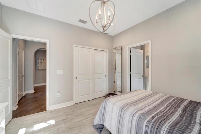 bedroom featuring arched walkways, a chandelier, visible vents, a closet, and light wood-type flooring