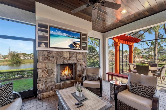 sunroom featuring ceiling fan, an outdoor stone fireplace, vaulted ceiling, and wood ceiling