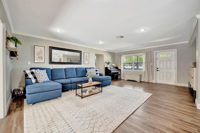 living area with baseboards, wood finished floors, visible vents, and crown molding