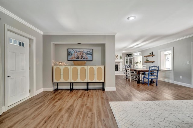 foyer with a fireplace with raised hearth, crown molding, baseboards, and wood finished floors