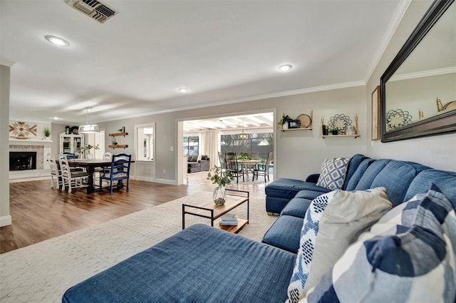 living room with a fireplace, visible vents, wood finished floors, and ornamental molding