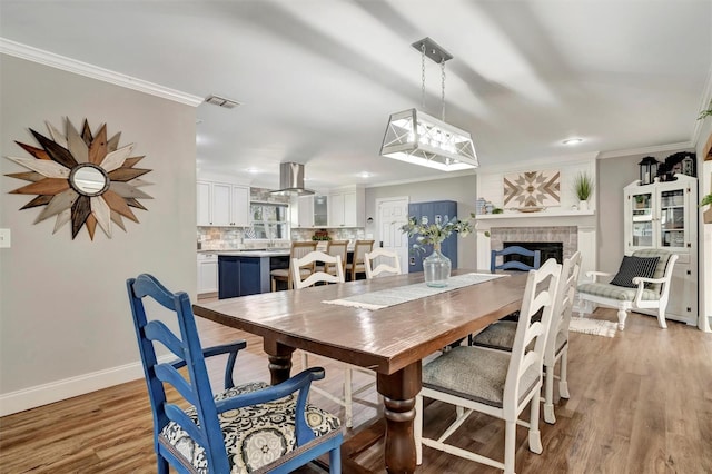 dining room with a fireplace, visible vents, baseboards, light wood-type flooring, and crown molding