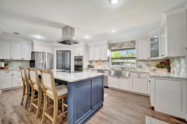 kitchen with a kitchen breakfast bar, island exhaust hood, stainless steel appliances, white cabinetry, and a sink