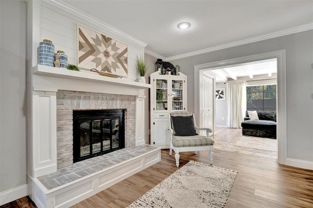 sitting room with a brick fireplace, crown molding, baseboards, and wood finished floors