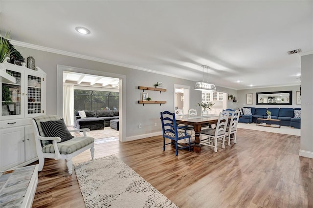 dining room featuring ornamental molding, light wood-style flooring, visible vents, and baseboards