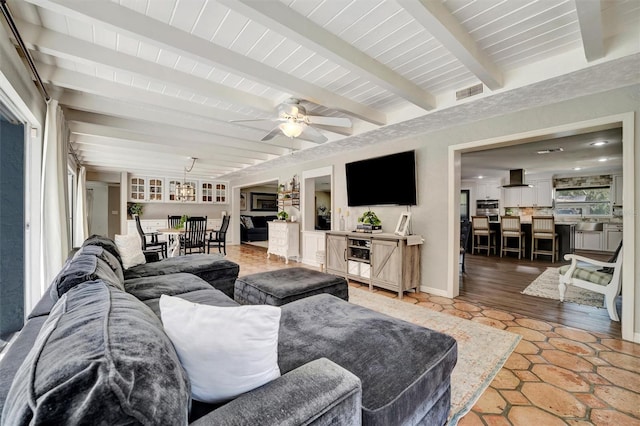 living area with a ceiling fan, baseboards, visible vents, and beam ceiling