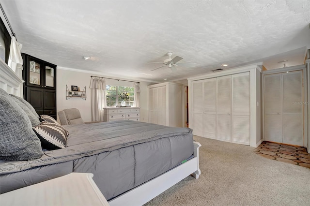 carpeted bedroom featuring a textured ceiling, ceiling fan, ornamental molding, and multiple closets