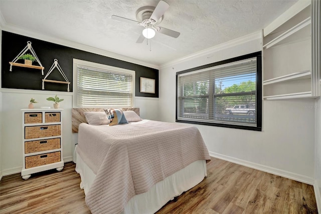 bedroom with ornamental molding, a textured ceiling, baseboards, and wood finished floors