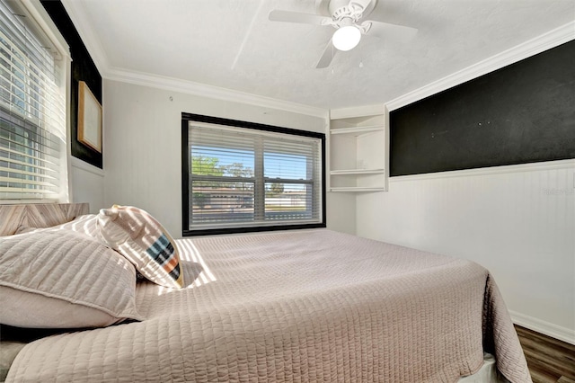 bedroom with wood finished floors, wainscoting, crown molding, and ceiling fan