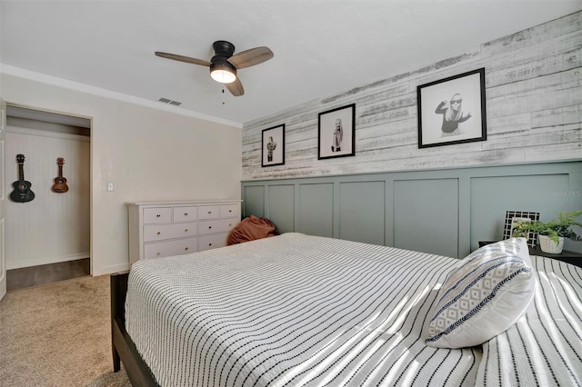 bedroom with visible vents, ceiling fan, carpet, crown molding, and a decorative wall