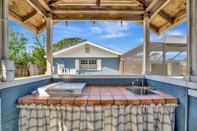 view of patio featuring glass enclosure, a sink, and fence