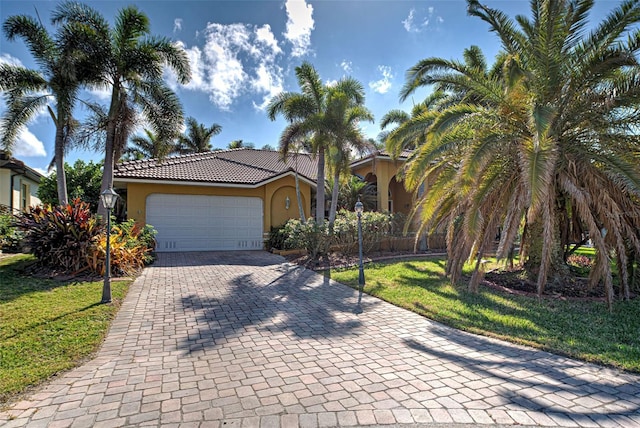 view of front of house with a garage, stucco siding, a tile roof, decorative driveway, and a front yard