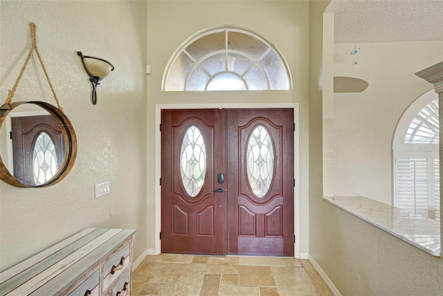 entrance foyer with baseboards, a textured wall, a textured ceiling, and stone tile floors