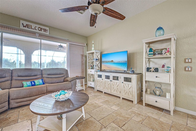 living room featuring baseboards, ceiling fan, a textured ceiling, and stone tile floors