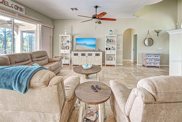 living room featuring a ceiling fan, arched walkways, stone tile flooring, and visible vents