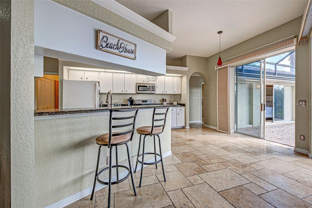 kitchen featuring arched walkways, decorative light fixtures, appliances with stainless steel finishes, white cabinetry, and a peninsula