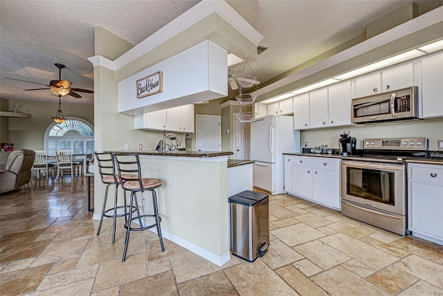 kitchen featuring a sink, white cabinets, appliances with stainless steel finishes, a kitchen bar, and stone tile flooring