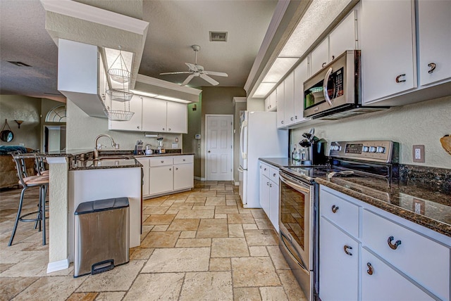 kitchen featuring visible vents, a breakfast bar, stainless steel appliances, white cabinetry, and a sink