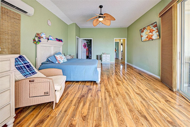 bedroom with light wood finished floors, a ceiling fan, an AC wall unit, a textured ceiling, and baseboards