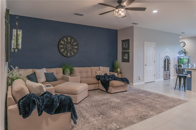 tiled living area featuring ceiling fan, an accent wall, visible vents, and baseboards