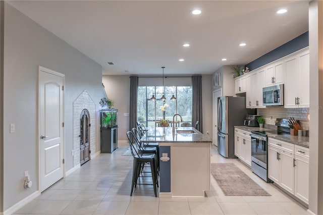 kitchen with a sink, white cabinetry, appliances with stainless steel finishes, tasteful backsplash, and a center island with sink