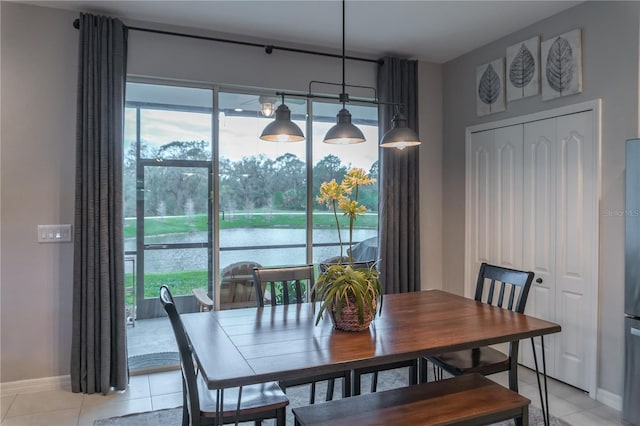 dining space featuring a healthy amount of sunlight, a water view, baseboards, and light tile patterned flooring