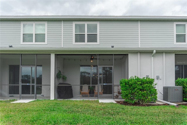 rear view of house with cooling unit, a sunroom, and a lawn