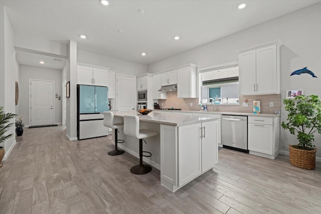 kitchen featuring stainless steel appliances, white cabinets, a kitchen island, and under cabinet range hood