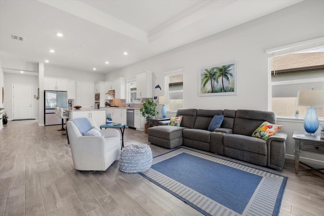 living area with visible vents, light wood-style flooring, ornamental molding, a tray ceiling, and recessed lighting