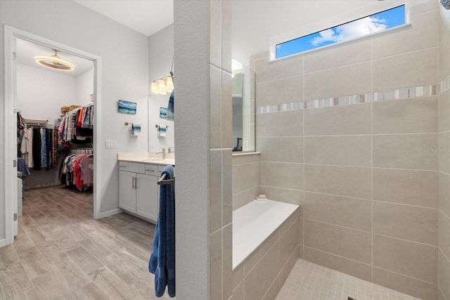 full bath featuring a walk in closet, vanity, wood finished floors, baseboards, and walk in shower