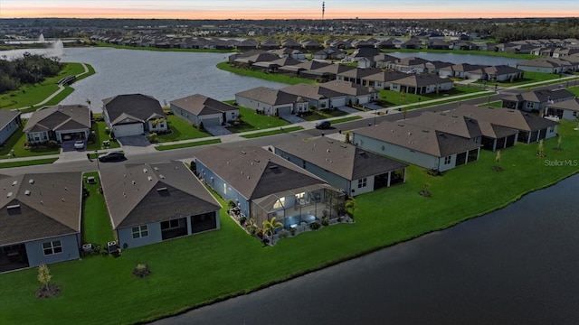 aerial view at dusk with a water view and a residential view