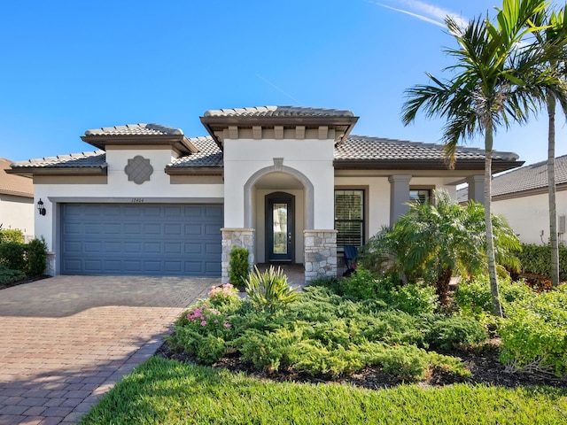 mediterranean / spanish-style house featuring a tiled roof, decorative driveway, an attached garage, and stucco siding