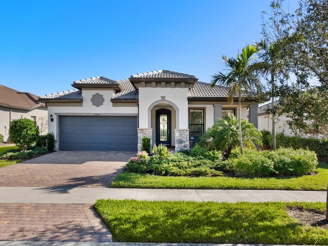 mediterranean / spanish-style home featuring a garage, a tile roof, stone siding, decorative driveway, and stucco siding