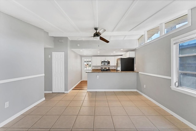 interior space featuring baseboards, white cabinets, stainless steel microwave, freestanding refrigerator, and a peninsula