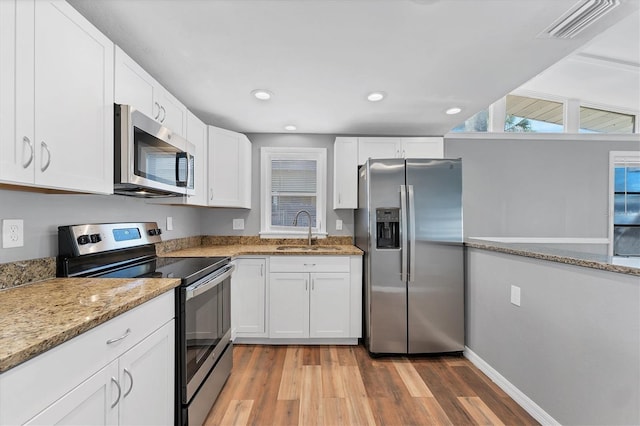 kitchen featuring stainless steel appliances, a sink, visible vents, white cabinets, and light stone countertops