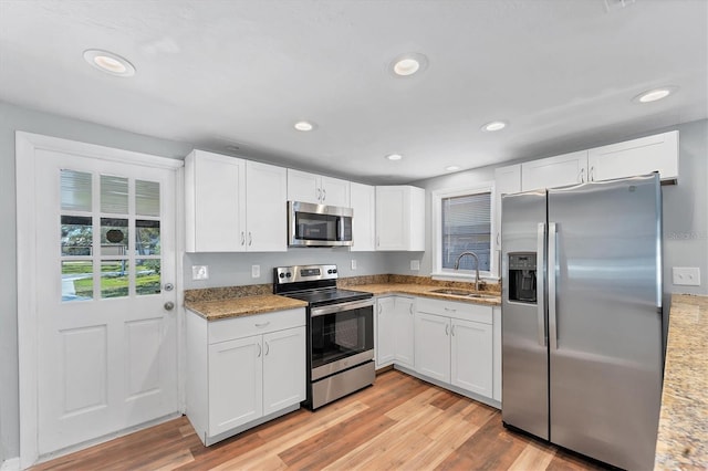 kitchen with light stone counters, light wood finished floors, appliances with stainless steel finishes, white cabinets, and a sink