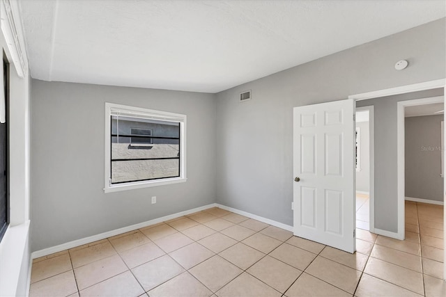 empty room with light tile patterned flooring, visible vents, and baseboards