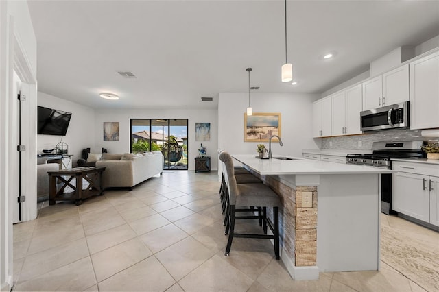 kitchen featuring pendant lighting, light countertops, appliances with stainless steel finishes, open floor plan, and a kitchen island with sink