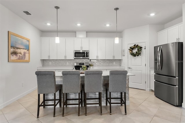 kitchen featuring white cabinets, an island with sink, appliances with stainless steel finishes, hanging light fixtures, and light countertops