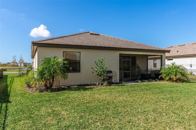 rear view of property with stucco siding, a yard, a tiled roof, and fence