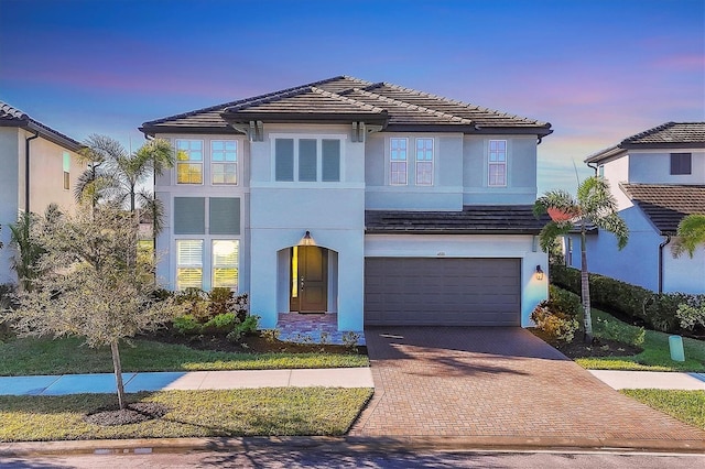 view of front of house featuring a tiled roof, decorative driveway, a garage, and stucco siding