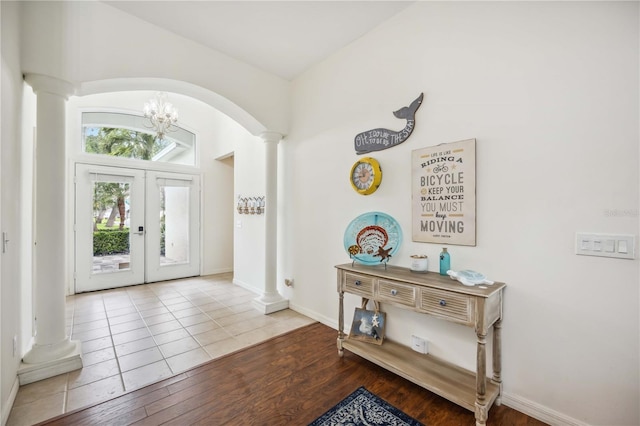 foyer entrance with arched walkways, french doors, decorative columns, wood finished floors, and baseboards