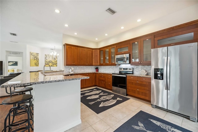 kitchen featuring light stone counters, stainless steel appliances, visible vents, a kitchen bar, and glass insert cabinets