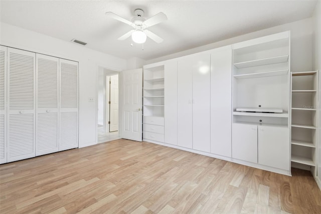 unfurnished bedroom featuring light wood-type flooring, a ceiling fan, visible vents, and two closets