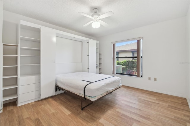 bedroom with a textured ceiling, ceiling fan, light wood-style flooring, and baseboards